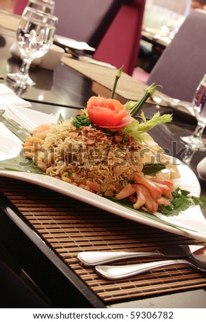A plate of Malaysian fried rice with garnishing, herbs, sliced tomato, raisins and banana leaf