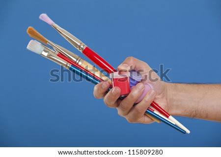 Hand holding several brushes and paint