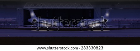 Two private planes in front of a hangar at night
