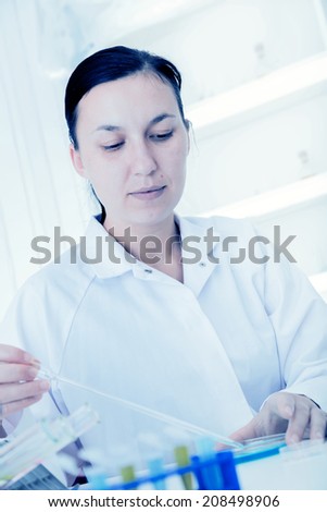 Young female researcher using microscope in the chemistry lab with laboratory glassware on background.