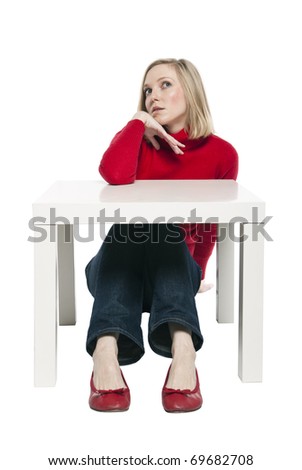 Young woman, office worker or student sitting at funny small desk. Studio photo, isolated.