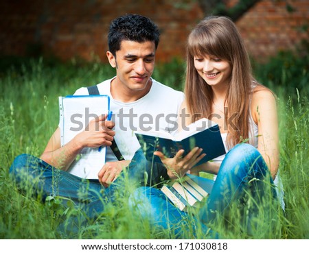 Two students guy and girl studying in park on grass with book outdoors