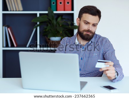 Young bearded man working on a laptop in the office - pays by credit card online shopping