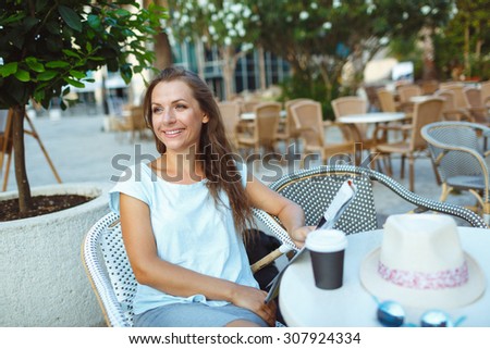 Young woman relaxing in the outdoor cafe - drinking coffee and reading the newspaper
