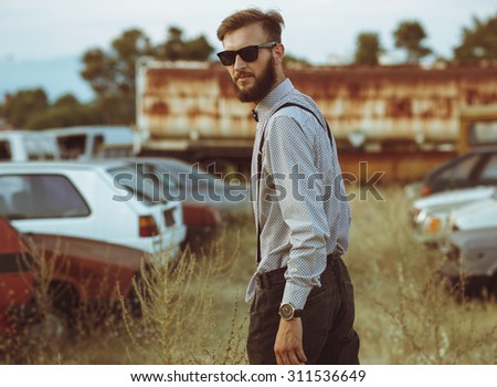 Portrait of a young handsome stylish man, wearing shirt and bow-tie on the field of old cars