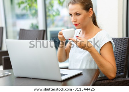 Young attractive business woman sitting in a cafe with a laptop and drinks her morning coffee