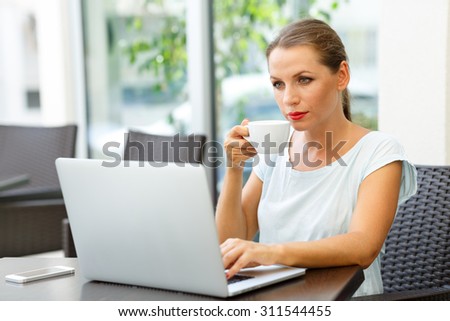 Young attractive business woman sitting in a cafe with a laptop and drinks her morning coffee