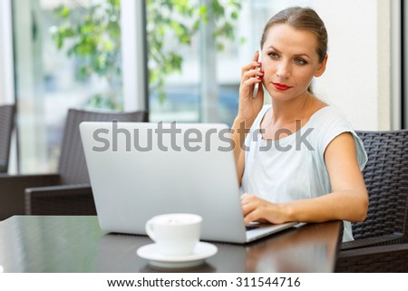 Attractive young woman sitting in a cafe with a laptop and talking on the cell phone