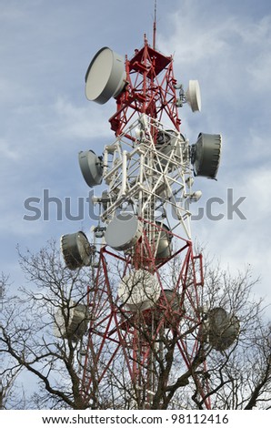 Telecommunication tower with satellite dishes and antennas above the trees.