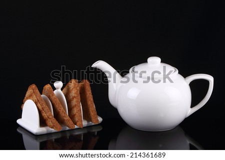 Four pieces of toast in a porcelain toast rack with white porcelain teapot.