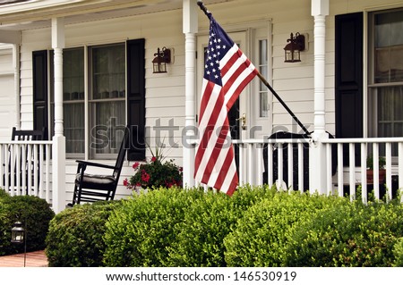 front porch of white colonial home with black shutters and american flag