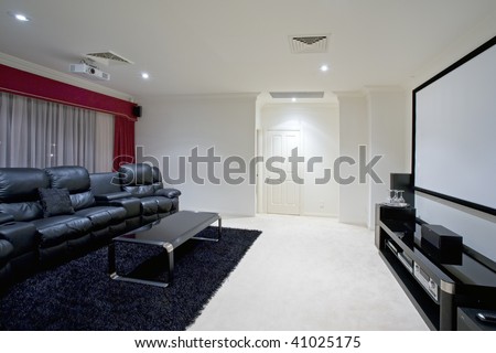 home theater room with black leather recliner chairs, red curtains, black rug and table with wine glasses and projector screen on wall