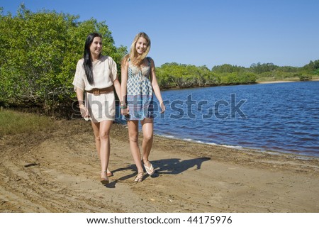 two girls holding hands walking and giggling by the creek