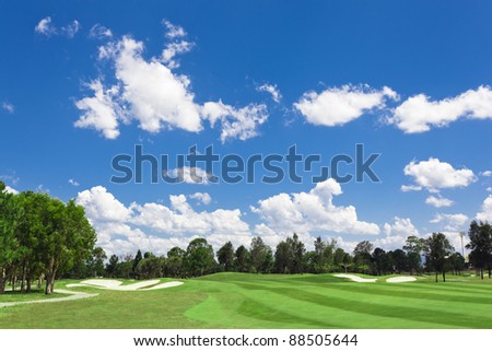 Sunny golf green with scattered clouds on a blue sky and forest