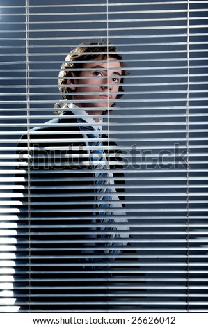 Young businessman behind a window blinds looking up