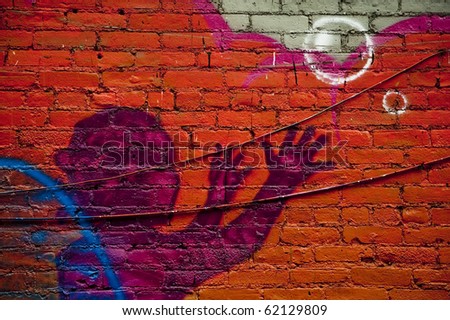Graffiti wall in urban centers depicts a kid and bubbles with arms raised upwards in purple on a bright orange wall with ridges and black telephone wires running across the breadth of the shot