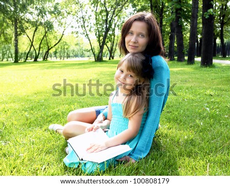 Portrait of little girl reading a book in the park with her mother