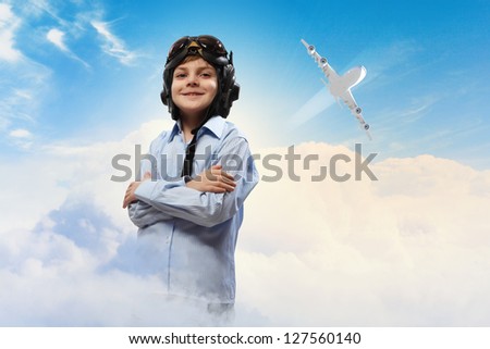 Image of little boy in pilots helmet with flying airplane in background