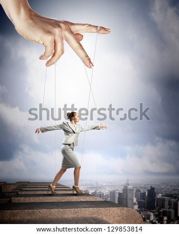 Businesswoman marionette on ropes controlled by puppeteer against city background