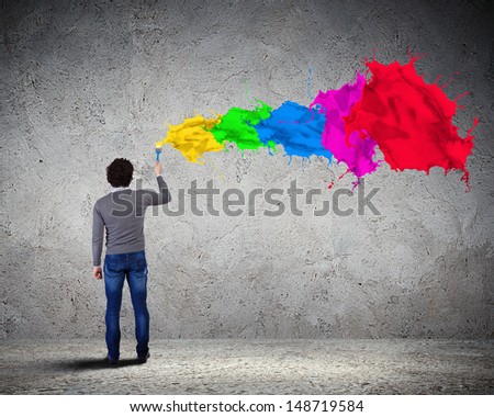 Young man spraying colour paints over background