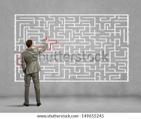 Back view image of young businessman trying to find way out of maze