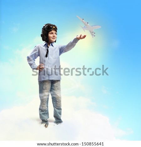 Image of little boy in pilots helmet playing with toy airplane against clouds background