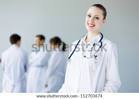 Attractive female doctor in white uniform with colleagues at background