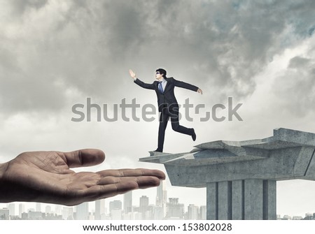 Image of running businessman at the edge of bridge supported by human hand