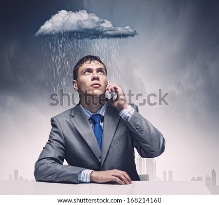 Businessman sitting under rain talking on mobile phone