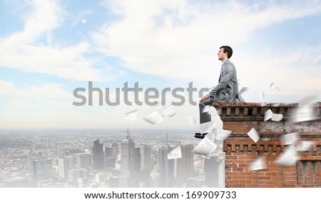 Young handsome businessman sitting at the edge of building roof