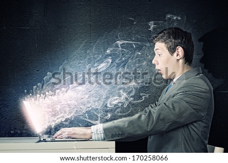 Young man in suit looking astonished in laptop. Surfing the internet