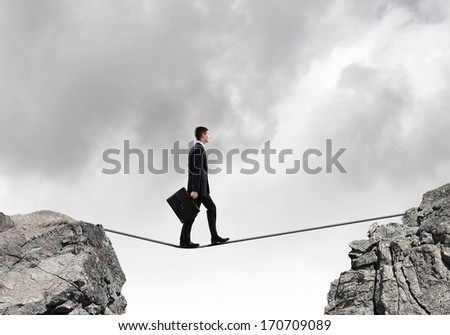 Conceptual image of businessman walking on rope above gap