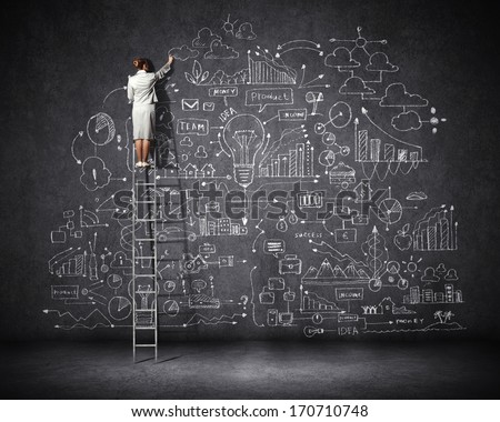 Rear view of businesswoman standing on ladder and drawing business sketch on wall