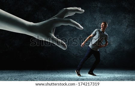 Funny image of young man trying to escape from huge hand