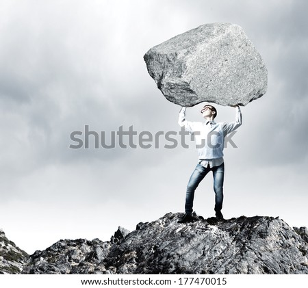 Young strong man holding huge stone above head