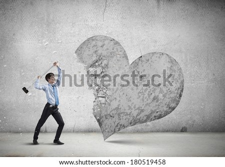 Young businessman breaking stone heart with hammer