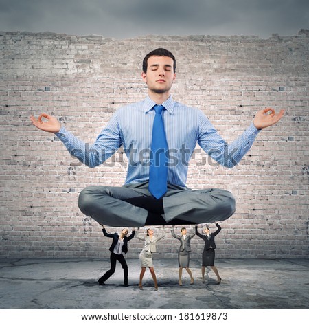 Young businessman sitting in lotus pose and supported by colleagues