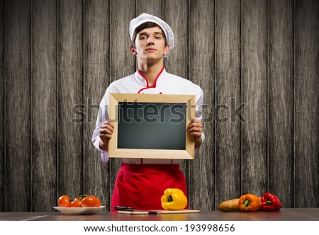 Handsome cook holding blank chalk board. Place for text