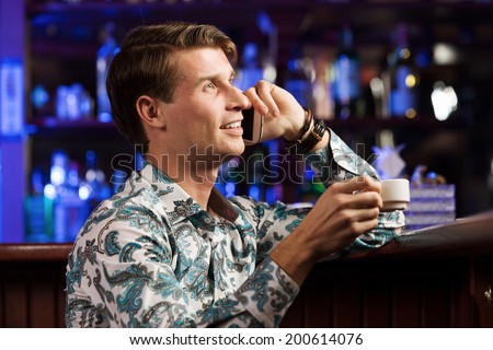 Young handsome man in casual sitting at bar and talking on phone