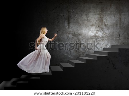 Young woman in white long dress walking up the staircase