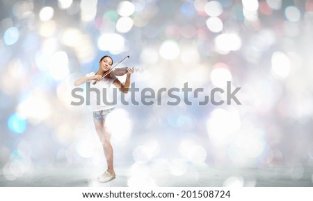 Young attractive woman playing violin with bokeh lights at background