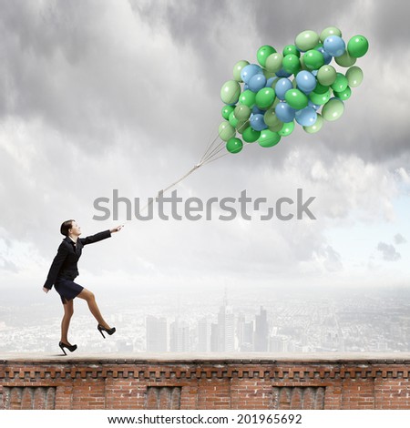 Young joyful businesswoman walking with bunch of colorful balloons