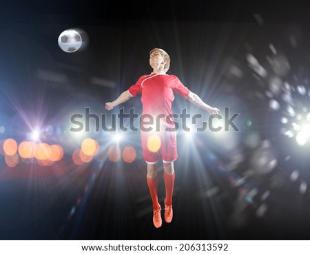 Young football player on stadium kicking ball with head in jump