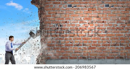 Young determined businessman with big hammer in hands crashing wall