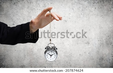 Close up of male hand holding alarm clock on rope