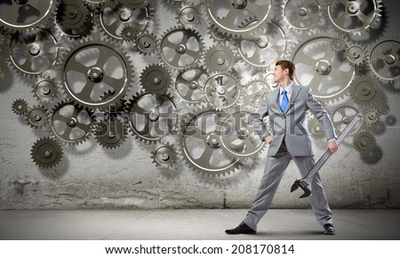 Young determined businessman with wrench in hands and cogwheels at background