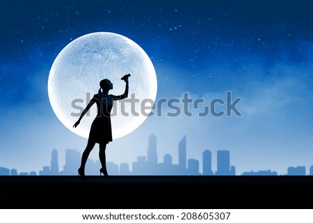 Silhouette of woman looking in binoculars with big full moon at background