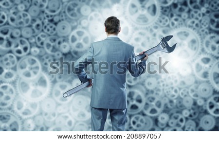 Rear view of determined businessman with wrench in hands and cogwheels at background