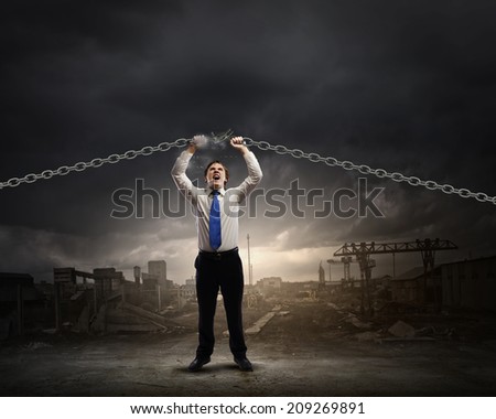 Young strong businessman tearing metal chain with hands
