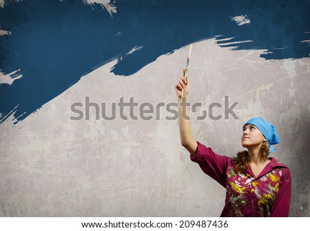 Young woman in headscarf painting wall with brush